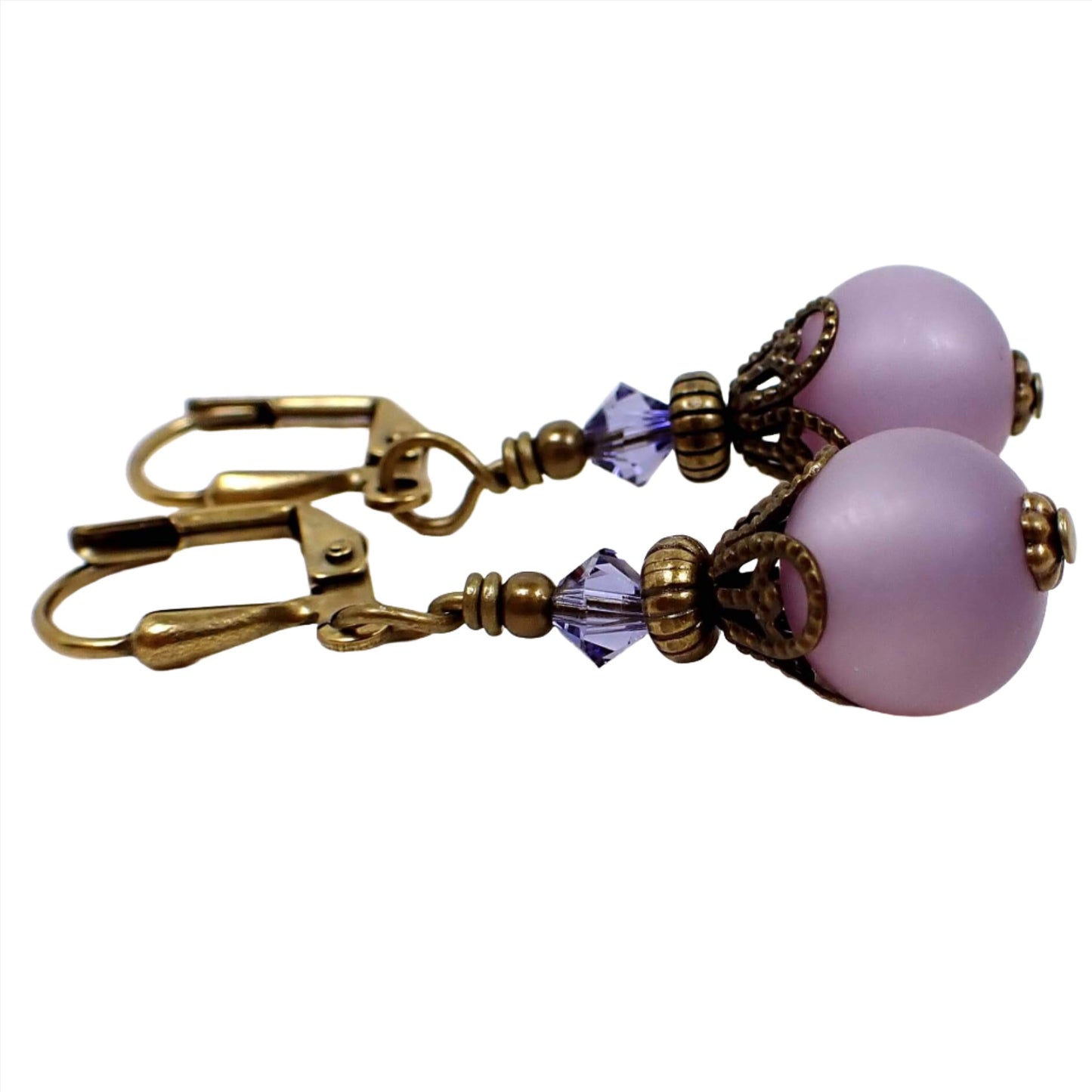 Side view of the small handmade frosted purple lucite drop earrings. The metal in antiqued brass in color. There is a purple glass faceted bead at the top and a round frosted matte purple lucite bead at the bottom.