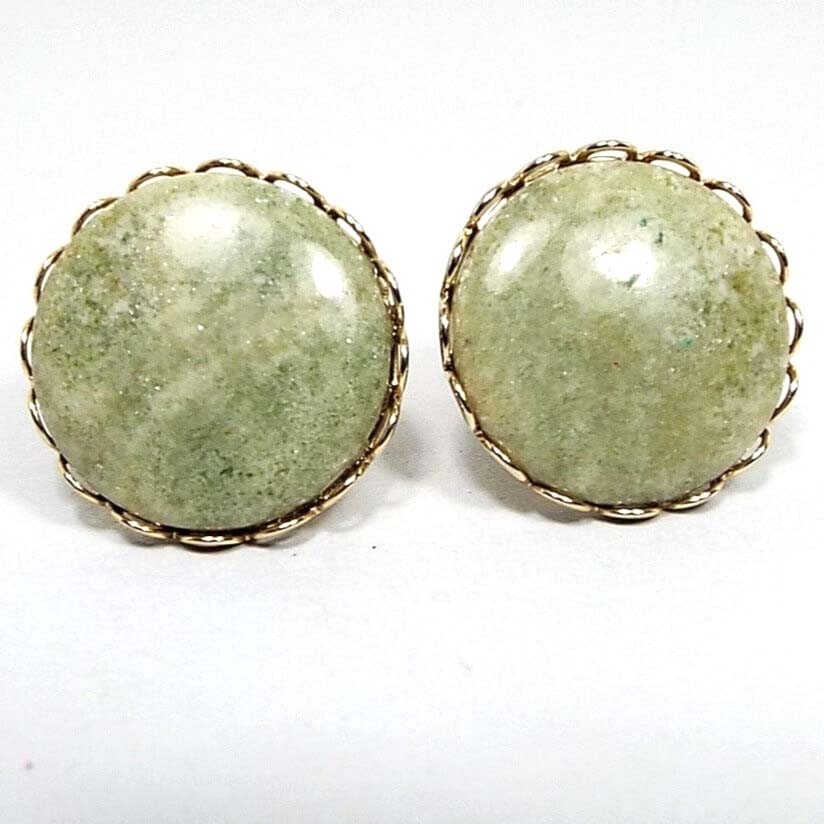 Front view of the retro vintage screw back gemstone earrings. The fronts have slightly domed serpentine cabs that are a light mossy green in color. The bezel edge has a cut out scalloped design. The metal is gold tone in color.
