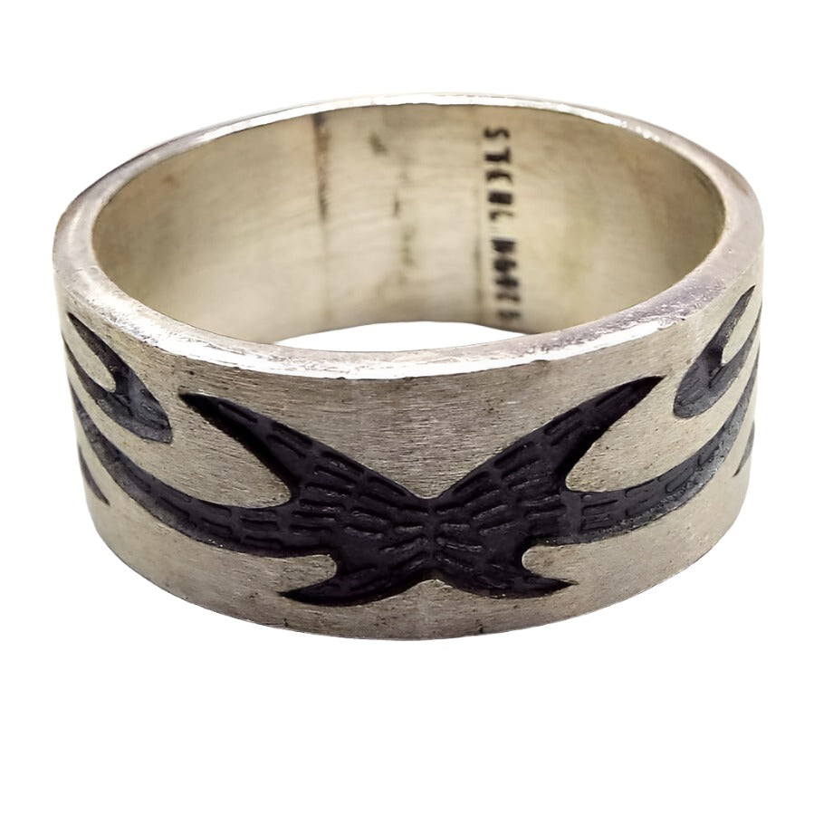 Angled front and side view of the retro vintage sterling silver band ring. The sterling is matte silver in color and the tribal style design is dark gray almost black in color. The design is curvy with spiky ends. Sterling 925 is stamped inside the band. There are some dark areas in side the band from age.