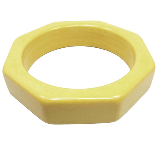 Angled top and side view of the Mid Century vintage Bakelite bangle bracelet. It has a thick octagon shape on the outside edge and the inside is smooth and round. The Bakelite is light butter yellow in color. 