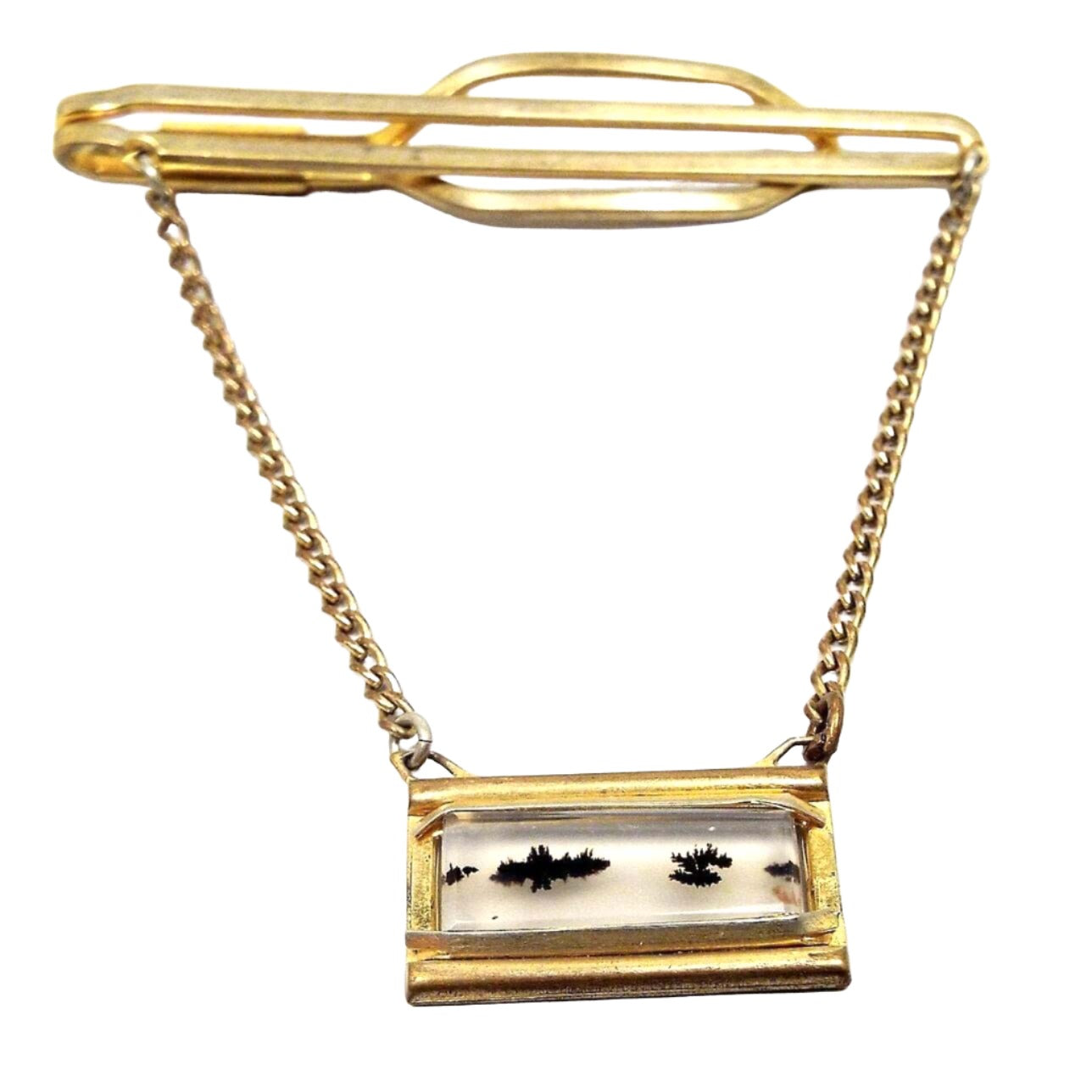 Front view of the 1940's Mid Century Nu Lok vintage tie bar chain. It has gold tone color metal. The bar at the top is a long open oval. It curves around to the back to form a larger open oval for a slide on style. Curb chain hangs from each side down to a rectangle charm that has a clear and black dendric agate gemstone slice in the middle. Most of the stone is clear with black splotch like areas going like a dotted line across the middle of the gemstone.