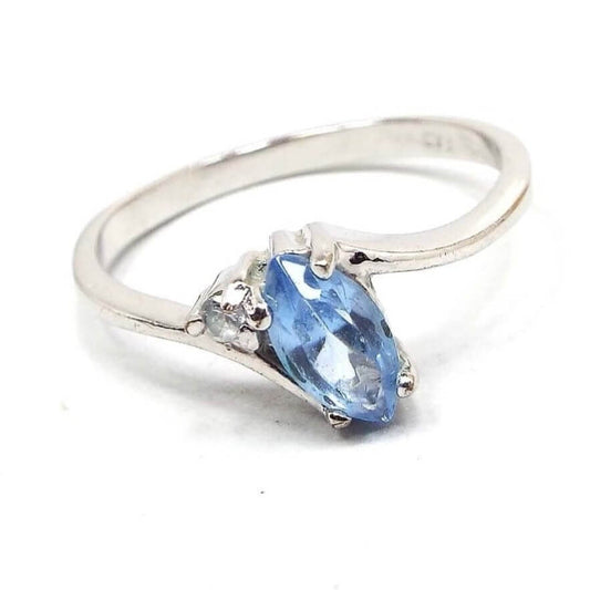Front view of the retro vintage rhinestone ring. The metal is silver tone in color. The top has a marquis cut light blue rhinestone that looks like an oval with pinched ends. There is a small round clear rhinestones by ones corner of the blue rhinestone. The band is thinner style and has a rounded outer edge. The inside is flat and smooth.