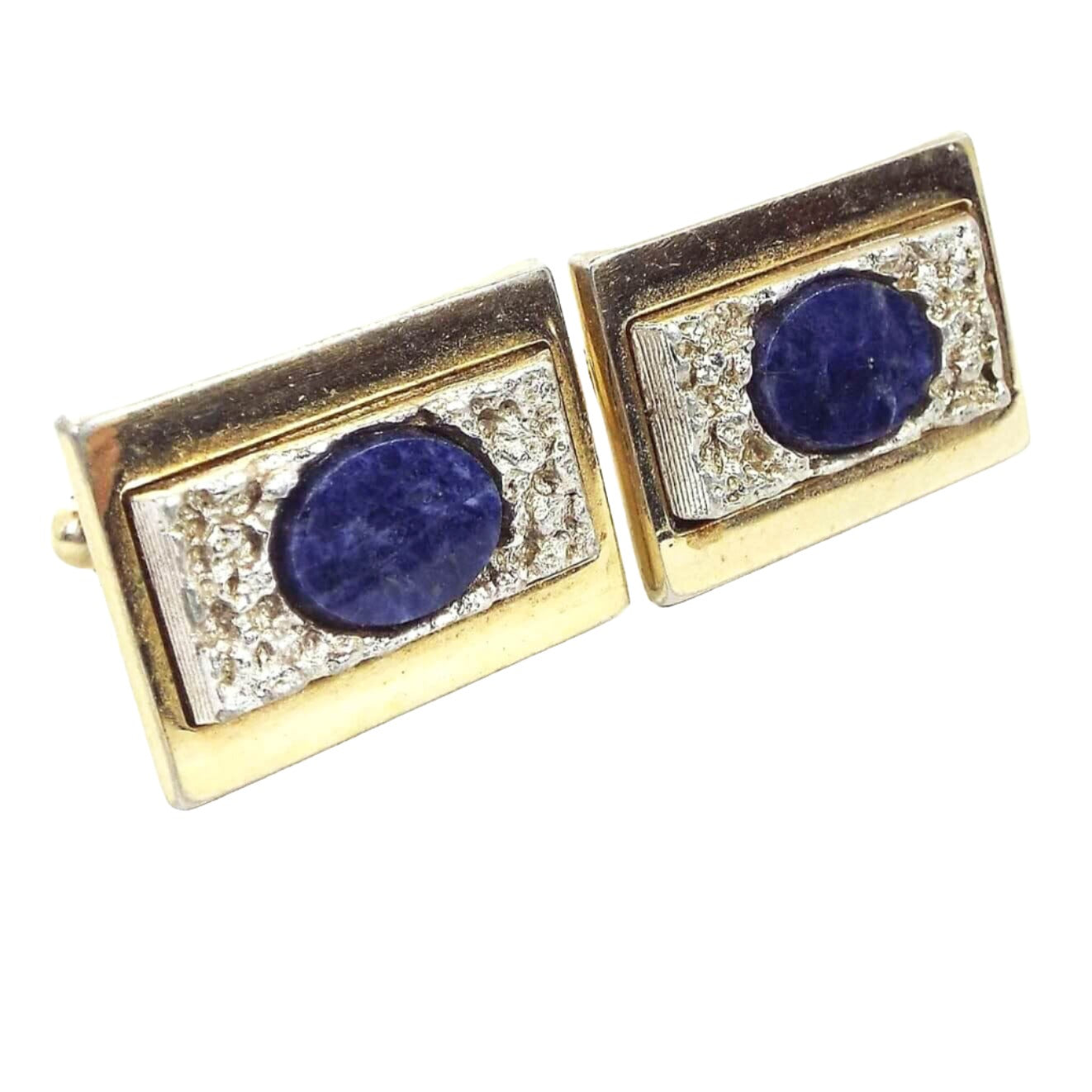 Angled front view of the retro vintage Anson sodalite cufflinks. The main color of the setting is gold tone. They are rectangular shaped with bumpy textured silver tone rectangles on the front. There are oval denim blue marbled sodalite gemstone cabs in the very middle.