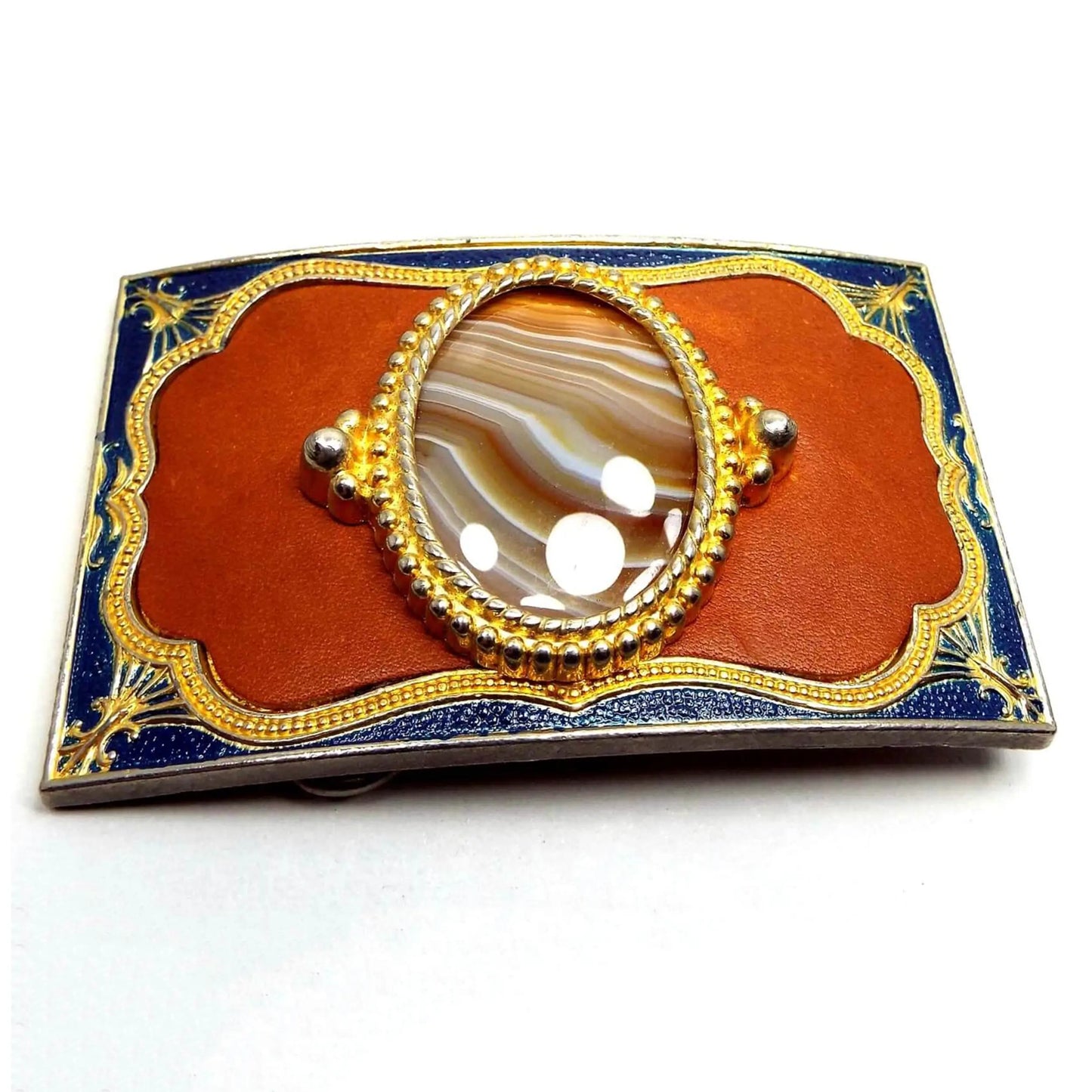 Front view of the retro vintage Southwestern style belt buckle. It is rectangle in shape with gold tone color metal. The outer edge is dark blue enameled. The inside area has dyed leather with an oval agate gemstone cab on top in shades of brown and white.