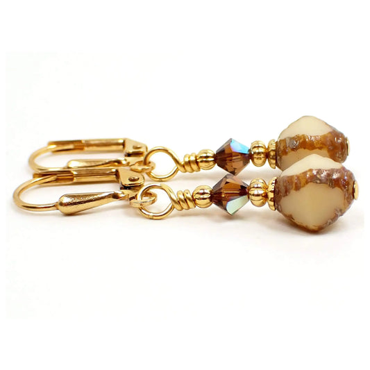 Enlarged side view of the small handmade drop earrings. The metal is gold plated in color. There are brown faceted glass beads at the top. The bottom Czech glass beads are bicone shaped and have brown with off white cut out areas on them.