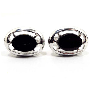 Front view of the retro vintage black and silver tone cufflinks. They are oval in shape. The middle has black glass cabs with a cut out style design around them.