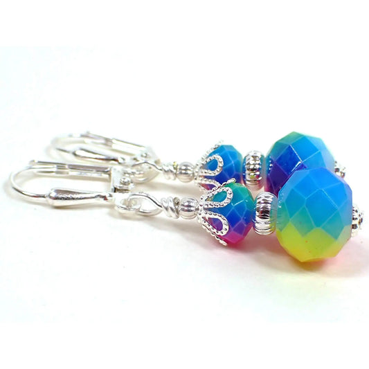 Angled side view of the handmade rainbow earrings. The metal is silver plated in color. There are faceted glass rondelle beads at the top and larger ones at the bottom. They having varying colors around the beads in rainbow colors.