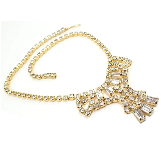 Front view of the retro vintage rhinestone necklace. The metal is gold tone in color. There is a strand of clear round rhinestones going down either side to a bottom middle pendant type area that's shaped kind of like a bow with clear round and clear baguette rhinestones.