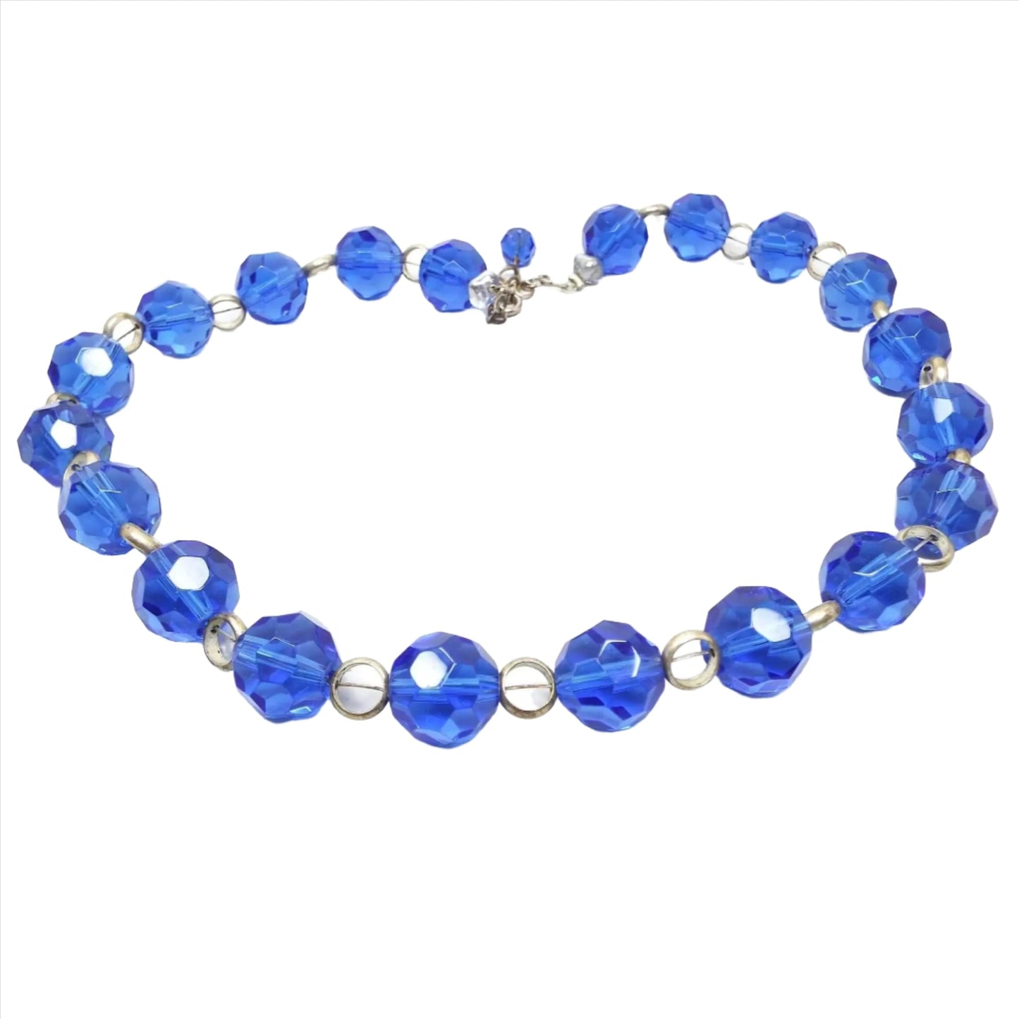 Top view of the Mid Century vintage glass beaded necklace. The beads are glass, faceted round, and blue in color. In between each bead is a matte silver tone open circle bead.