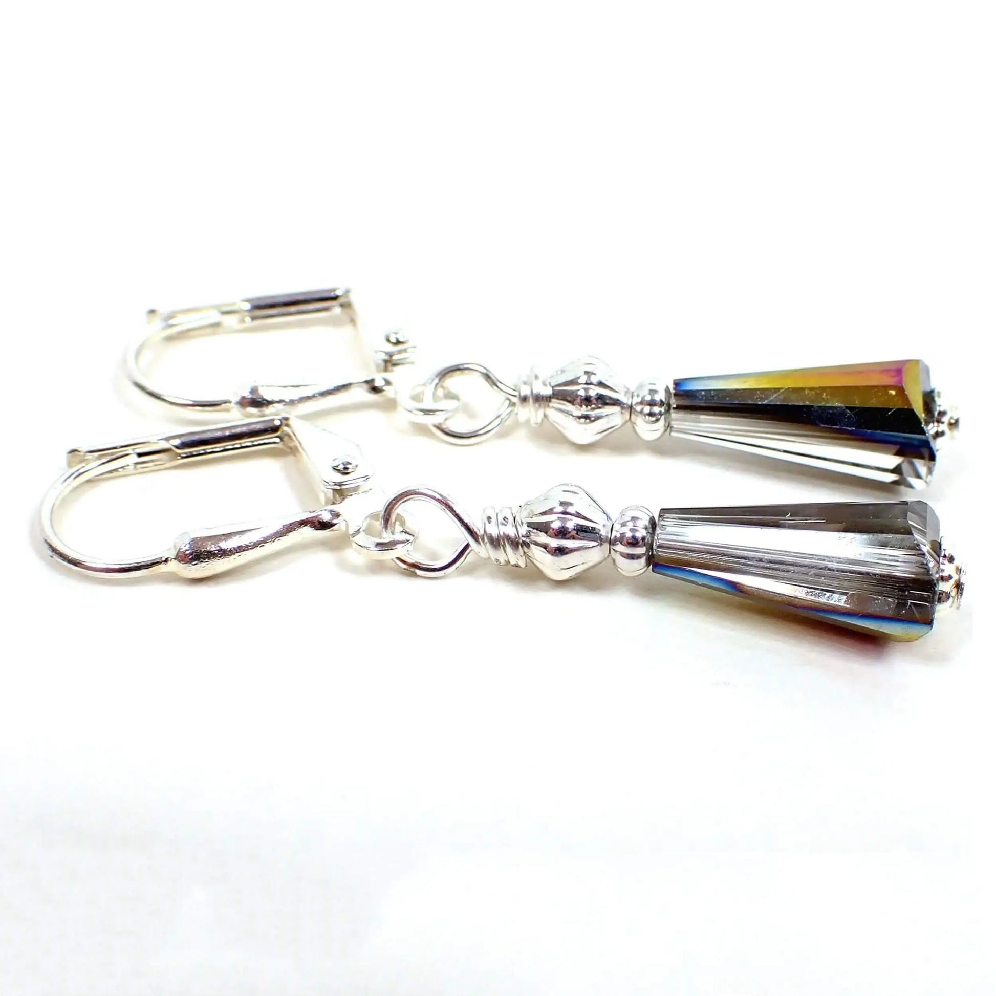 Angled view of the small handmade glass crystal beaded earrings. The metal is silver plated in color. There are faceted trapezoid shaped beads at the bottom that are clear with one half of the beads having a dark AB coating on them.