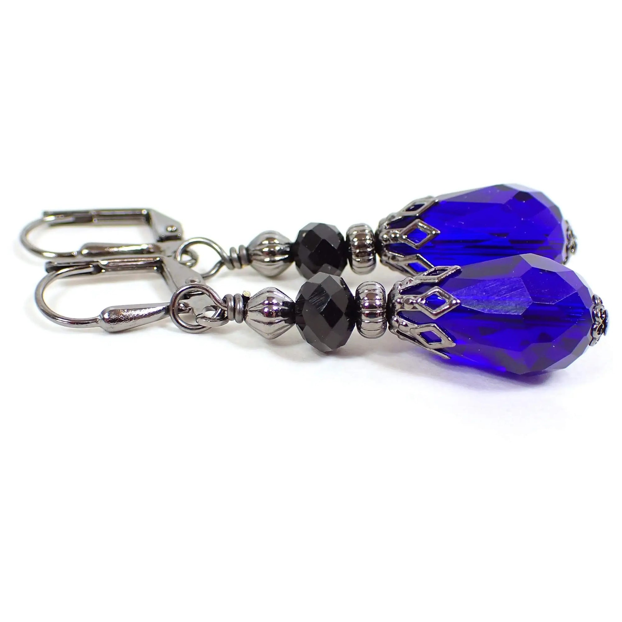 Side view of the handmade teardrop earrings. The metal is gunmetal gray in color. There are black faceted glass crystal beads at the top. The bottom beads are teardrop shaped faceted glass crystal and are a vibrant cobalt blue in color.