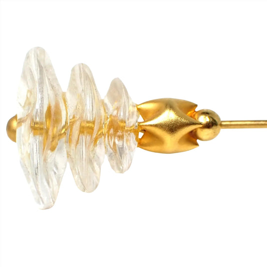 Enlarged side view of the top of the Mid Century modernist stick pin. The metal is gold tone plated in color. There is a clear plastic shape on the top that has three tiers of wavy disc like areas. There is a crimped gold tone bead below that.