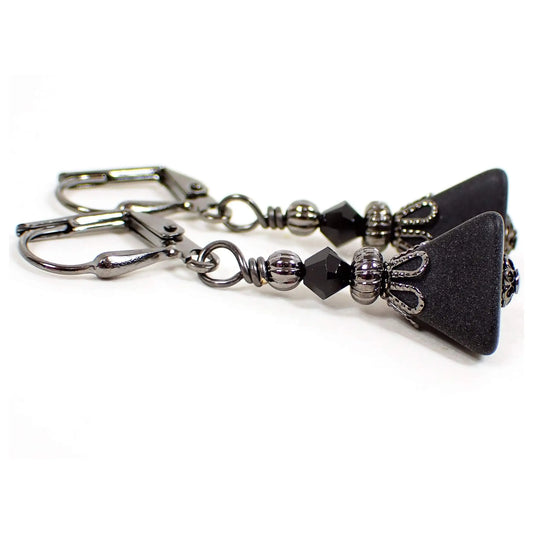 Side view of the handmade pyramid earrings. The metal is gunmetal gray in color. There are small black faceted glass beads at the top. The bottom vintage lucite beads are a dark gray in color and triangle shaped.
