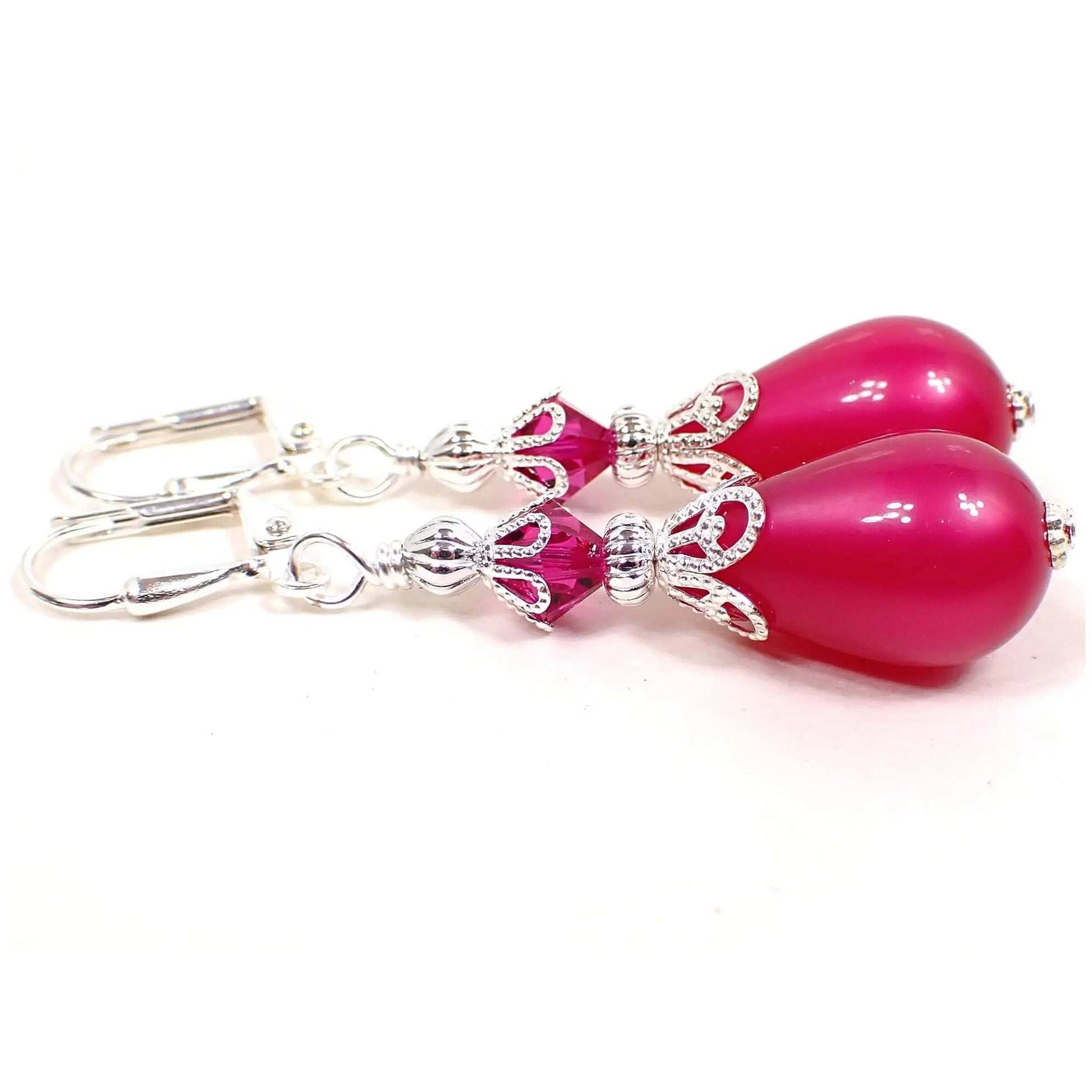 Side view of the handmade earrings with vintage moonglow lucite beads. The metal is silver plated in color. There are new faceted glass crystal beads in bright pink at the top. The bottom beads are vintage moonglow lucite with a bright raspberry pink color. They have an inner like glow as you move around in the light.