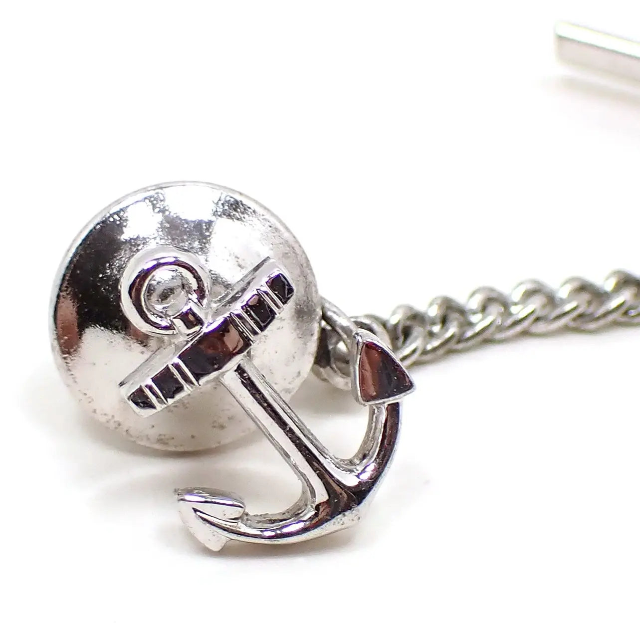 Enlarged front view of the retro vintage tie tack. It is silver tone in color and shaped like a boat or ship anchor. 