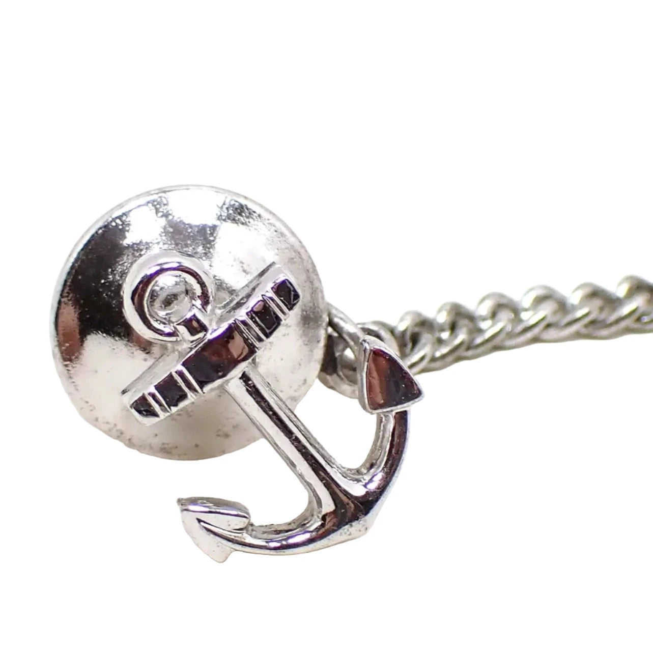 Enlarged front view of the retro vintage tie tack. It is silver tone in color and shaped like a boat or ship anchor. 