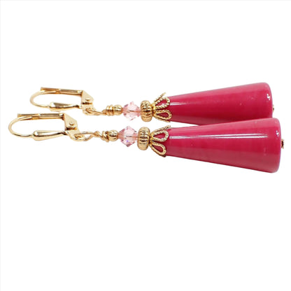 Side view of the handmade geometric cone earrings. The metal is gold plated in color. There are light pink faceted glass crystal beads at the top. The bottom beads are vintage lucite beads in a raspberry pink color.