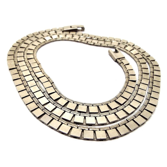 Angled view of the retro vintage square link chain necklace. It has a flat style link with squares on the bottom and thin textured rectangles on the top. There is a snap lock clasp at the end.