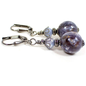 Side view of the handmade drop earrings with vintage lucite beads. The metal is gunmetal gray in color. There are periwinkle blue faceted glass beads on the top. The bottom lucite beads are round sphere shaped and are mostly purple with brown, orange, and white marbled in. Each bottom bead is different in appearance than the other for a unique look.