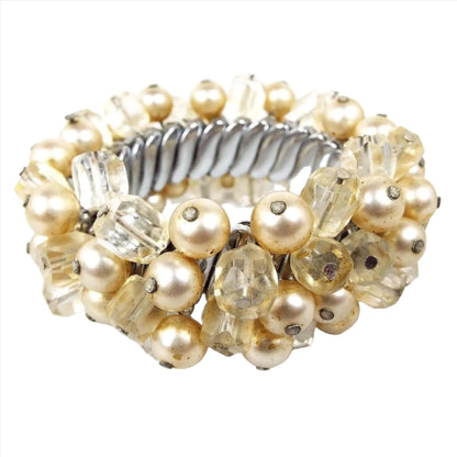 Angled side view of the Japan Mid Century vintage beaded expansion bracelet. The metal expansion links are silver tone in color. There are off white faux pearl beads and light yellow faceted glass crystal beads. The beads are clustered all the way around the bracelet.