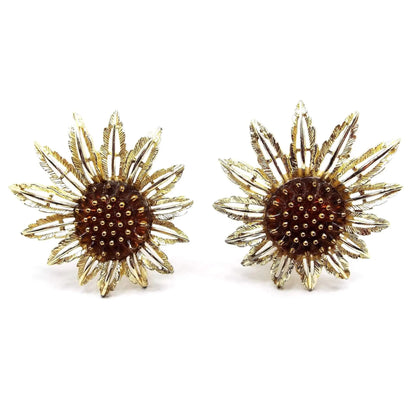 Front view of the Mid Century vintage Sarah Coventry "Starburst" flower earrings. The metal is gold tone in color. There are open cut out style petals with larger ones on one side and shorter on the other. The middle has a dark orange lucite cab with metallic gold painted tips.