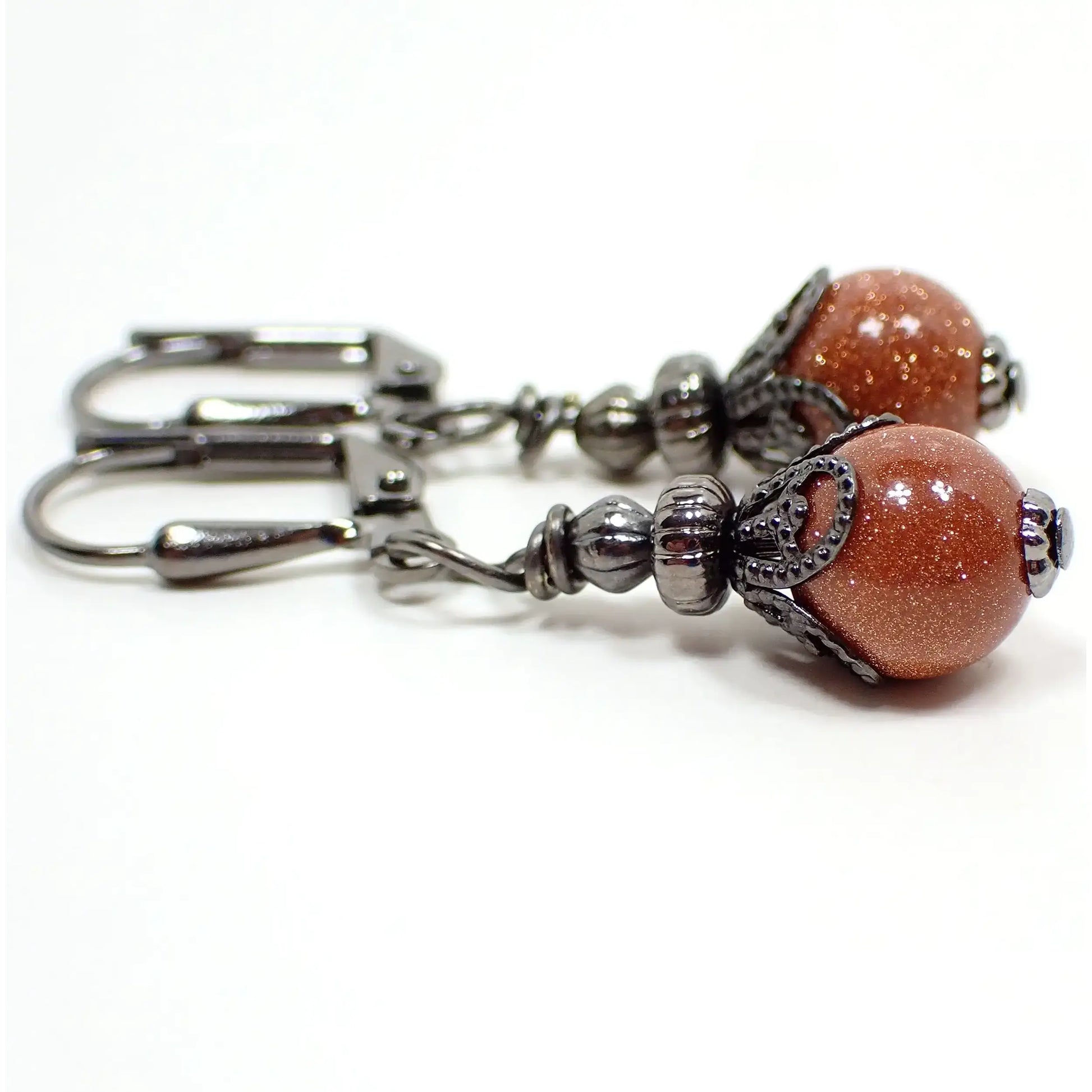 Side view of the handmade goldstone drop earrings. They have gunmetal gray color beads and findings. There are small round ball goldstone beads at the bottom. The goldstone beads are orange glass with tiny flecks of copper for sparkle.