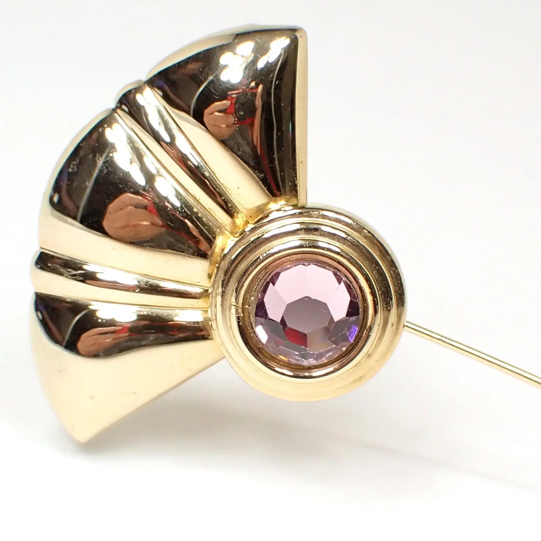 Enlarged view of the top of the retro vintage stick pin. It has a fan like shape on top that has a scalloped edge. Below that is a round area with a flat back rhinestone that is very light purple in color but has hues of pink as you move around and depending on the lighting.