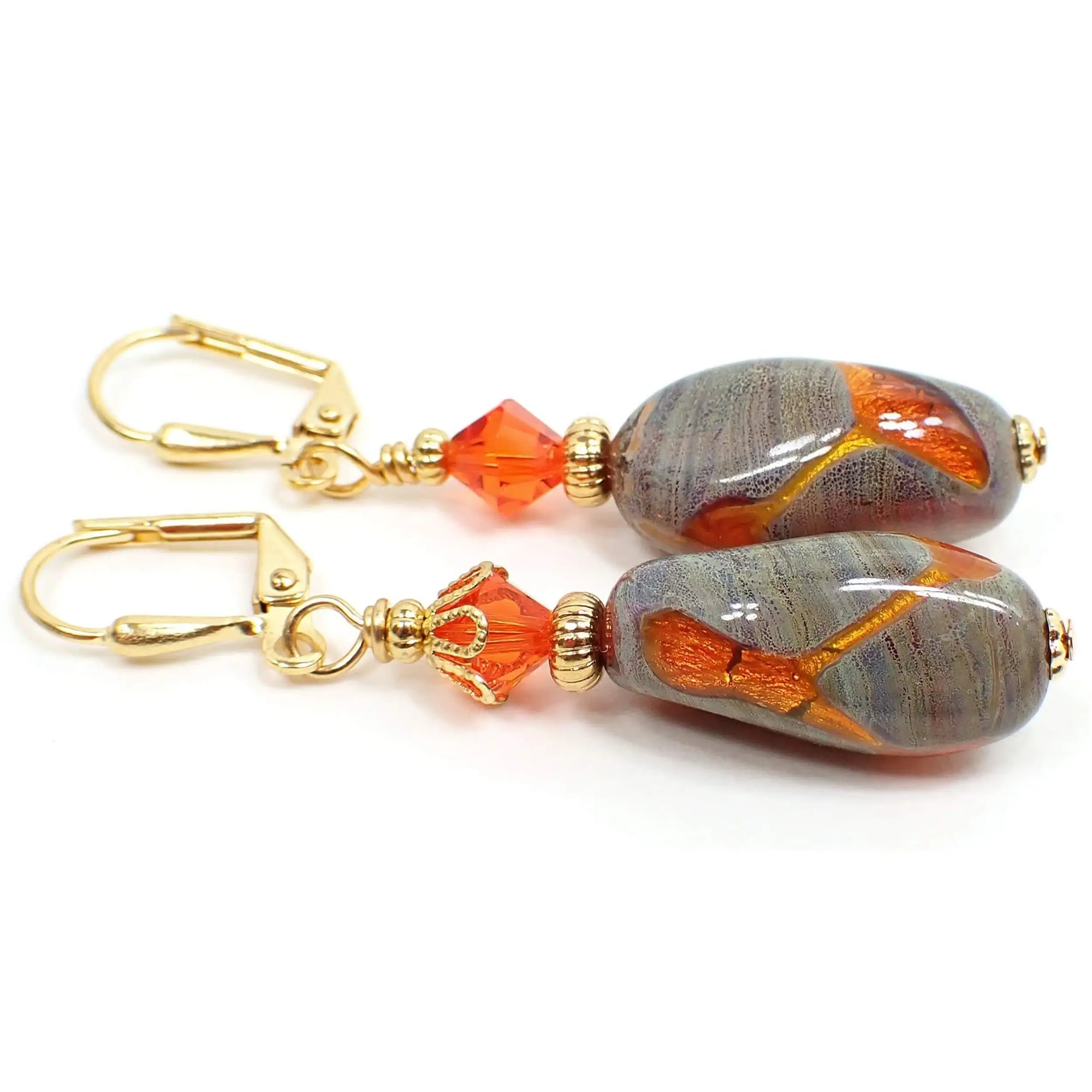 Side view of the handmade drop earrings with reclaimed vintage acrylic beads. The metal is gold plated in color. There are new bright orange faceted glass crystal beads at the top. The bottom vintage beads are acrylic and have a faux stone like appearance that is shades of green with lines. There are areas of bright orange in various places on the beads. Each bead is different than the other in the orange patterns.