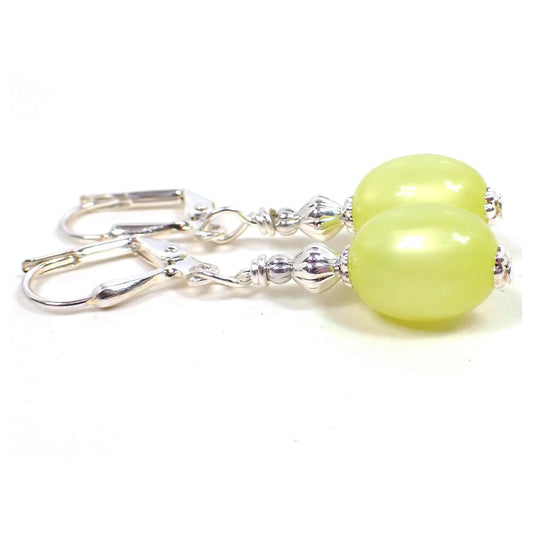 Side view of the small handmade drop earrings. The metal is silver plated in color. There are small vintage oval moonglow lucite beads in a light lemon yellow color. They have an inner like glow as you move around in the light.