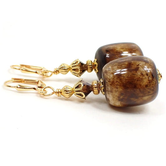 Side view of the chunky lucite handmade drop earrings. The metal is gold plated in color. There are brown faceted glass crystals at the top. The bottom beads are large barrel shaped and have shades of brown and off white.