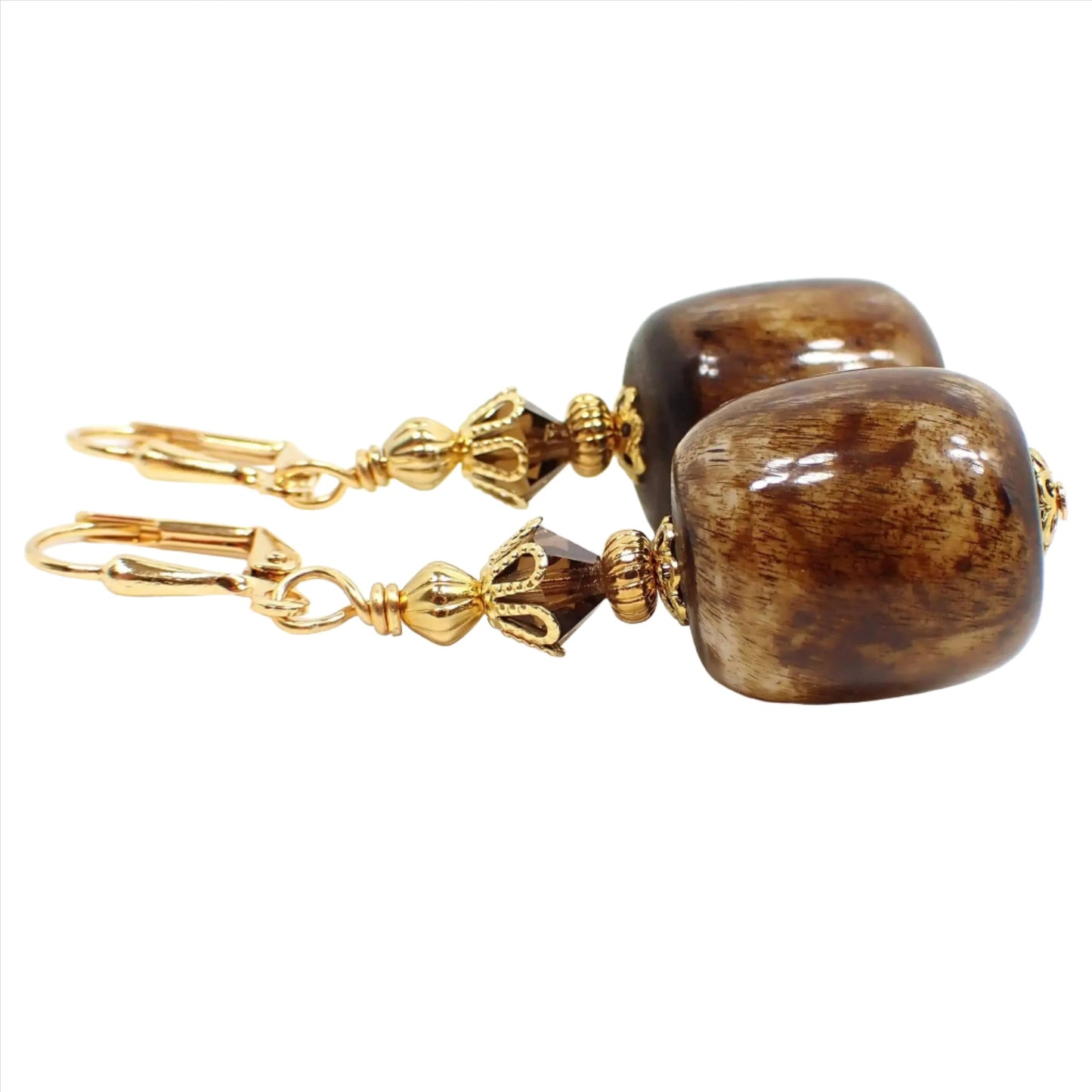 Side view of the chunky lucite handmade drop earrings. The metal is gold plated in color. There are brown faceted glass crystals at the top. The bottom beads are large barrel shaped and have shades of brown and off white.