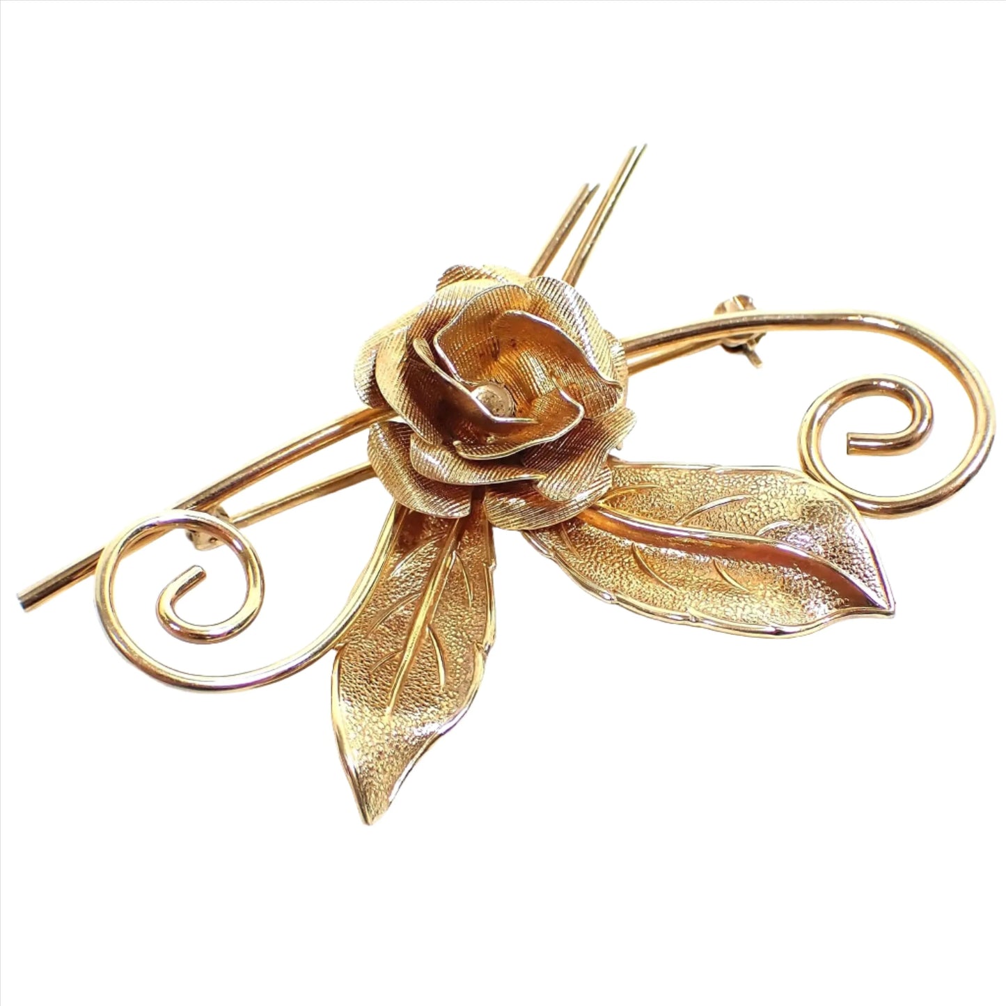 Angled front view of the Mid Century vintage Winard floral brooch pin. The metal is gold filled and a darker gold tone in color. There is a rose flower in the middle with two leaves coming off the bottom. Each side has a curled wire coming off of it. The leaves and flower petals are matte textured.
