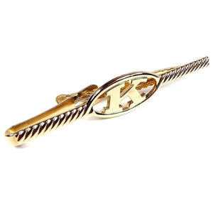 Front view of the retro vintage initial tie clip. It is gold tone in color with a twisted look design on the front. the middle area has an open oval with the letter K in it.