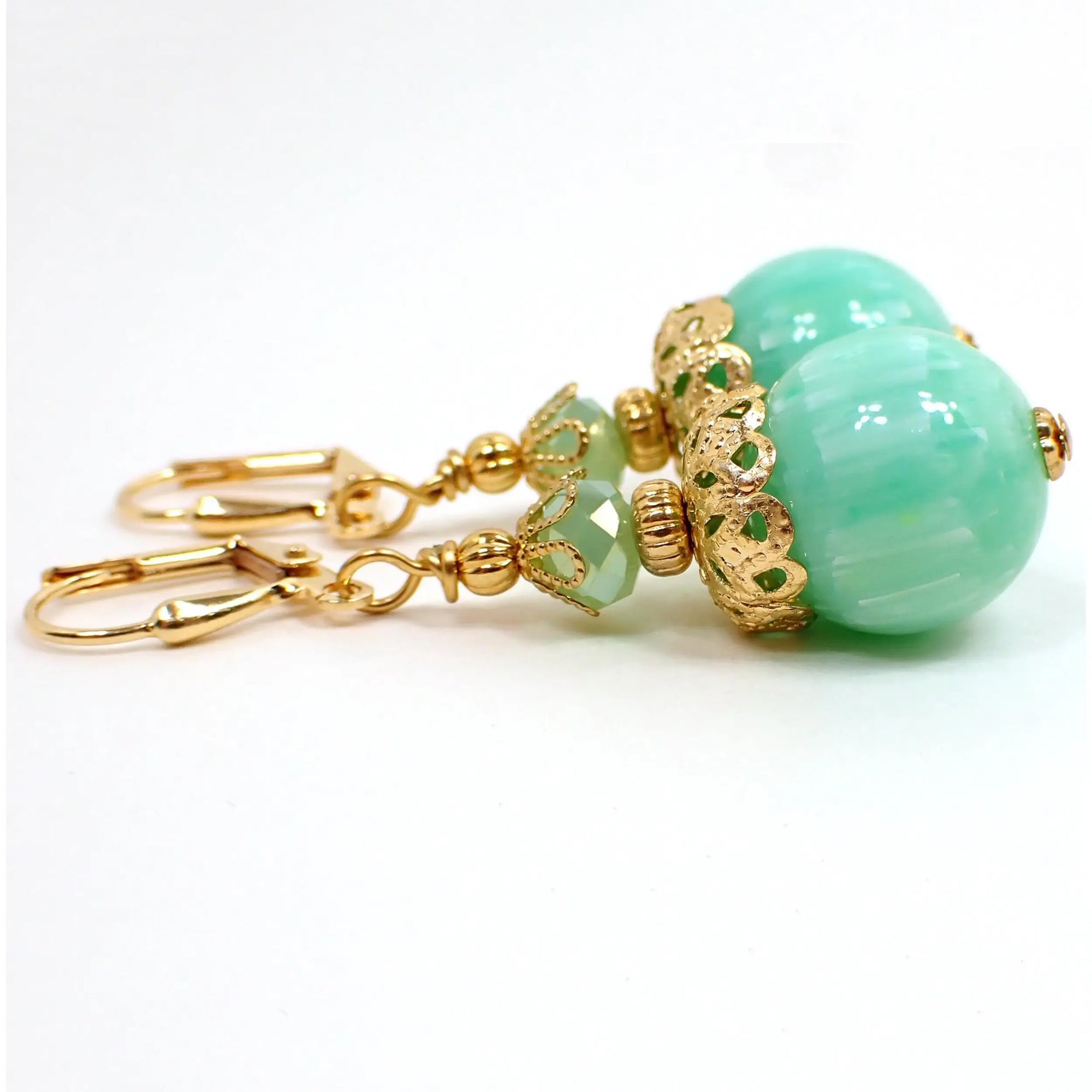 Side view of the handmade lucite drop earrings. The metal is gold plated in color. There are new faceted glass crystal beads in a light mint green color at the top. The bottom beads are vintage lucite and are round in sea foam green with thin white stripe pattern.