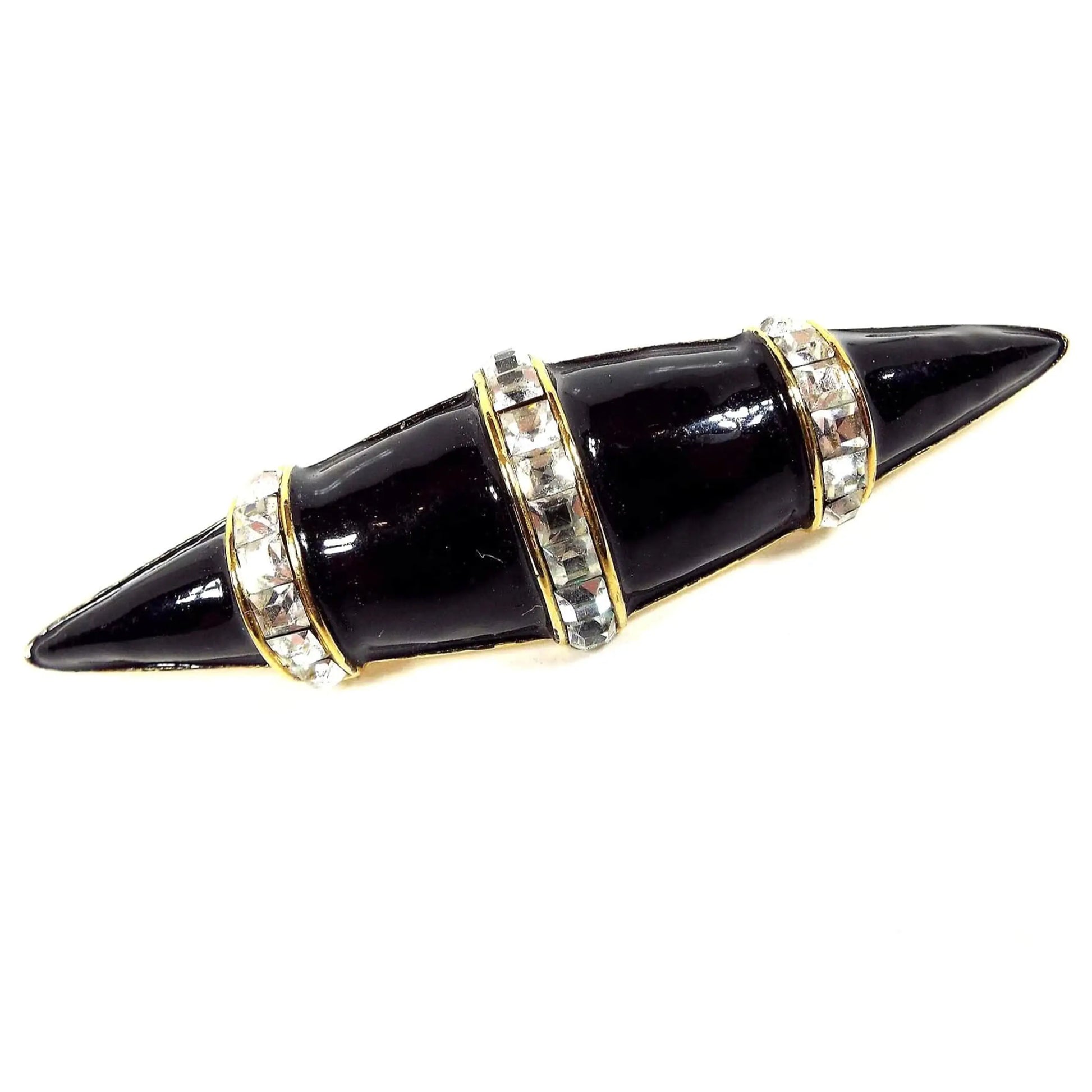 Front view of the retro vintage brooch pin. The metal is gold tone in color and it's shaped like an elongated oval with pointed edges. There are three bands of square clear rhinestones over the domed top. In between the bands and on the ends is black enameled.