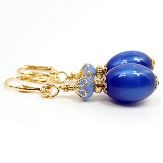 Side view of the handmade moonglow lucite earrings. The metal is gold plated in color. The to of the earrings have light blue faceted glass crystal beads. The bottom oval beads are vintage moonglow lucite beads in a deep blue color. They have an inner glow like appearance as you move around in the light.