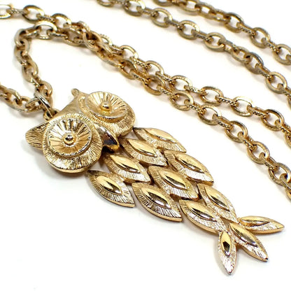 Enlarged front view of the retro vintage Avon pendant necklace. The metal is gold tone plated in color. The cable chain has textured oval links. The pendant is shaped like an owl with each layer jointed by rings on the back so it can move around as it hangs.