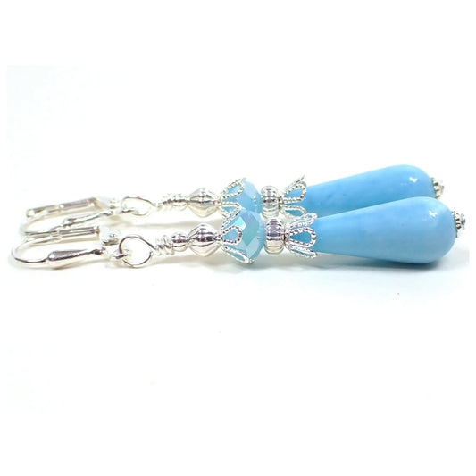 Side view of the handmade teardrop earrings vintage lucite beads. The metal is silver plated in color. There are light opaque blue faceted glass beads at the top. The bottom lucite beads are teardrop shaped and a baby blue in color.