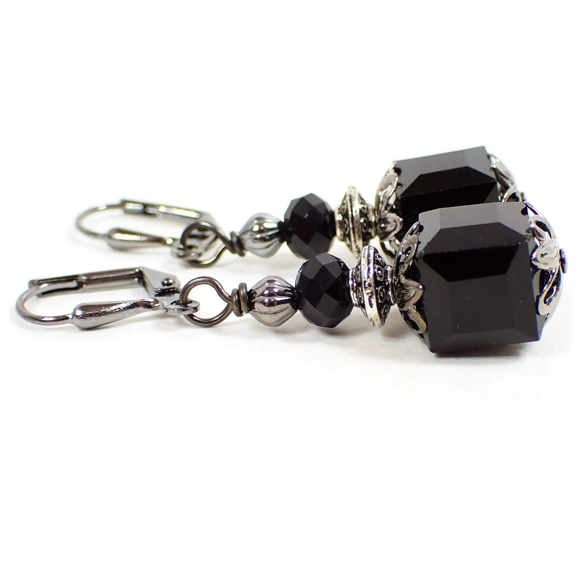 Side view of the handmade cube earrings. The metal is gunmetal gray in color. There are black faceted rondelle glass crystal beads at the top and black faceted glass crystal cube beads at the bottom.