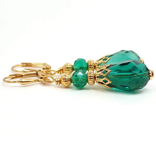 Side view of the handmade glass crystal teardrop earrings. The metal is gold tone in color. There is a faceted oval glass crystal teal green bead at the top and a teal green faceted glass crystal teardrop bead at the bottom.