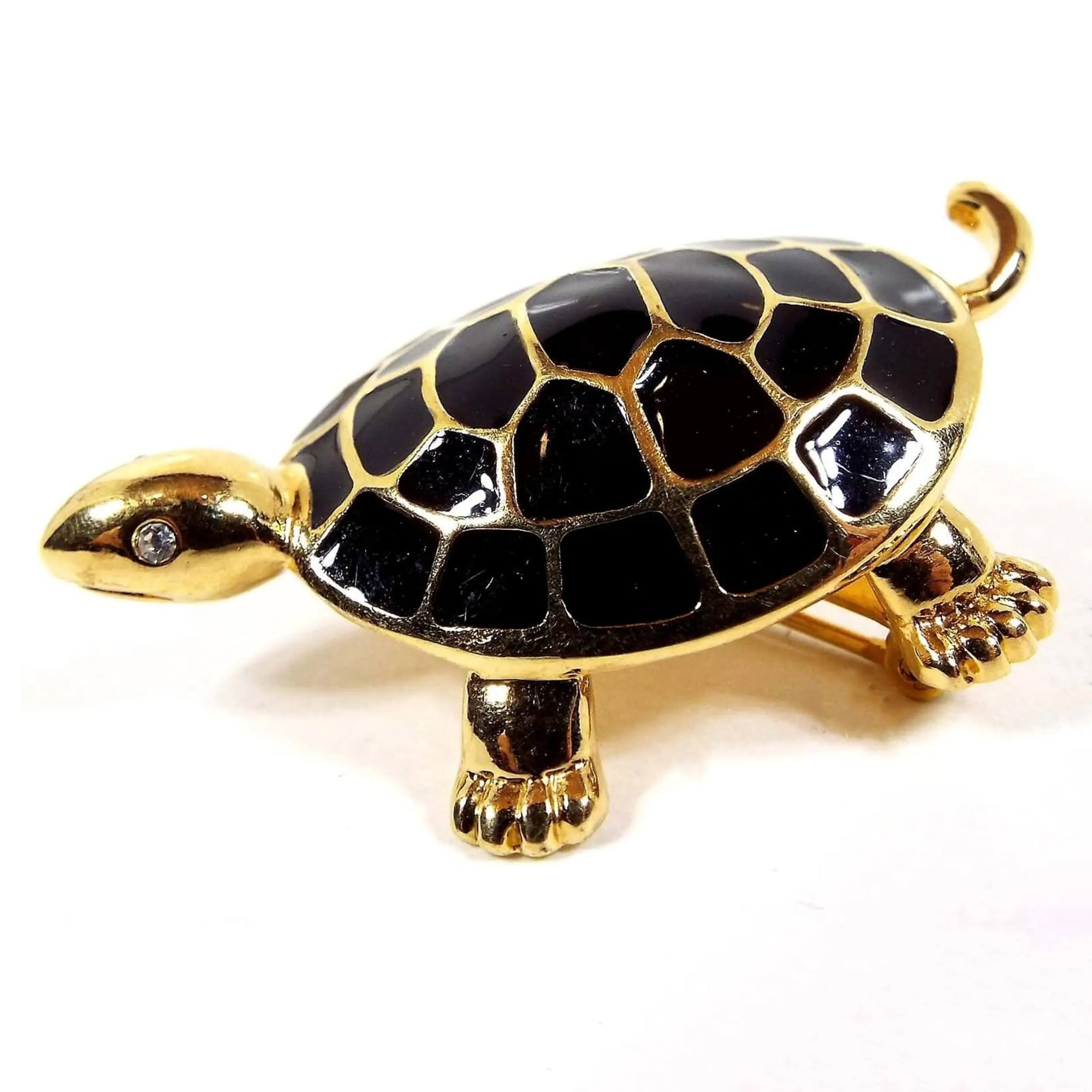 Side view of the retro vintage turtle brooch pin. The metal is gold tone in color. The turtle has clear rhinestone eyes and the pattern on his shell is black enameled.