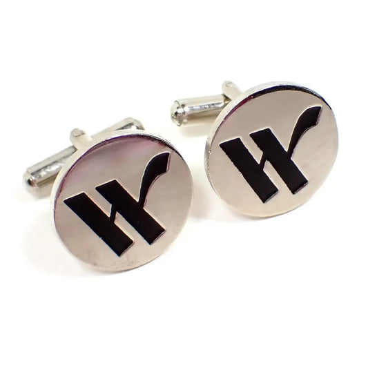Angled front view of the retro vintage initial cufflinks. They are round and silver tone in color. There is a fancy block style letter W on the front in black.