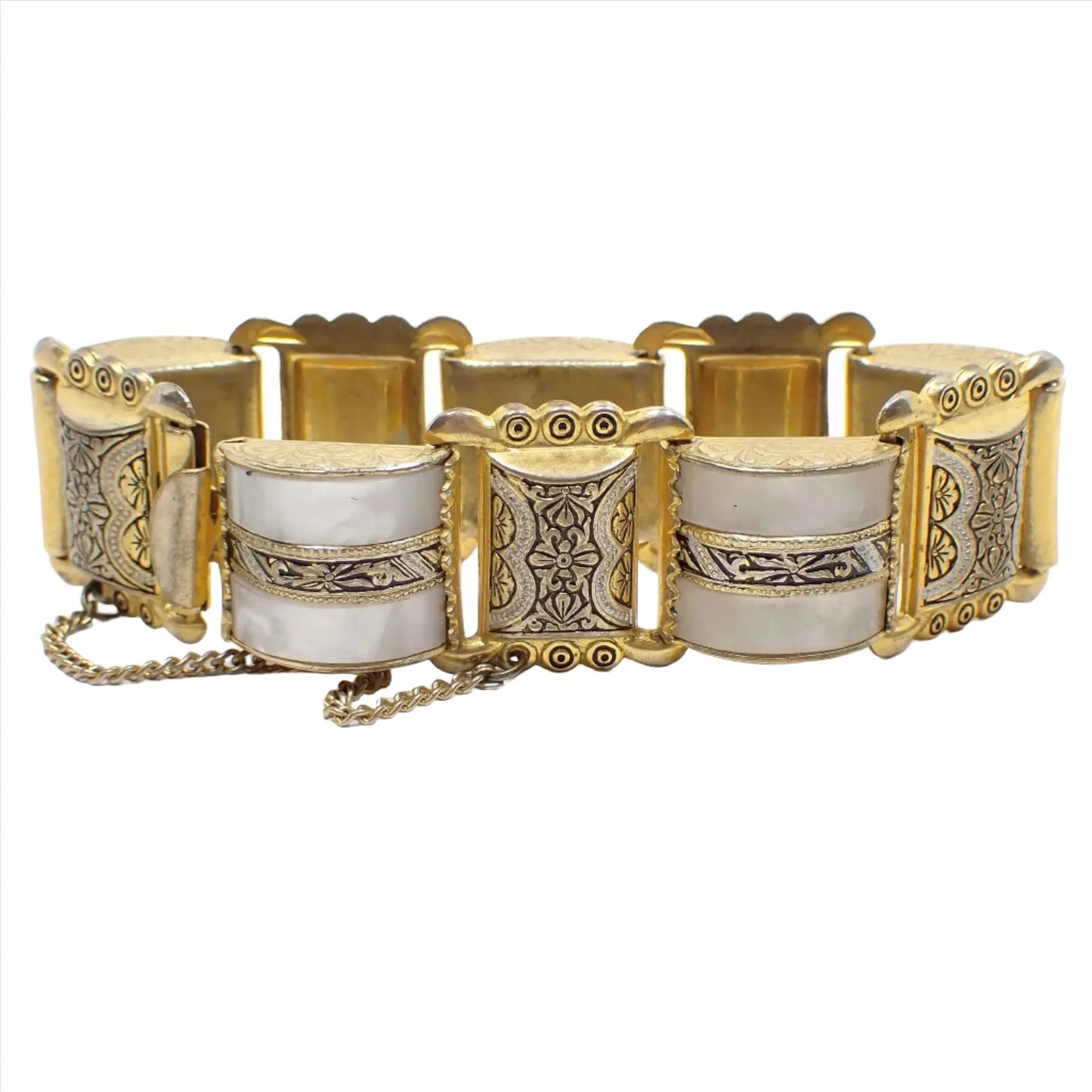 Enlarged view of the top of some of the links on the Mid Century vintage Damascene and lucite link bracelet. There are metal links with black and silver painted accents on the gold tone metal and in between them are domed links with pearly white lucite and painted metal strips in the middle. There is a safety chain and box clasp showing in the photo.