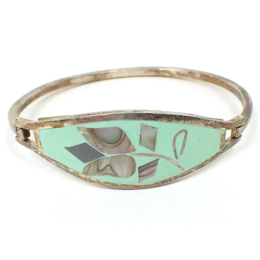 Front view of the retro vintage Mexican alpaca floral hinged bangle bracelet. The silver tone metal has a slightly darkened patina from age. The front is mint green enameled with a flower design made up of pieces of inlaid abalone shell.
