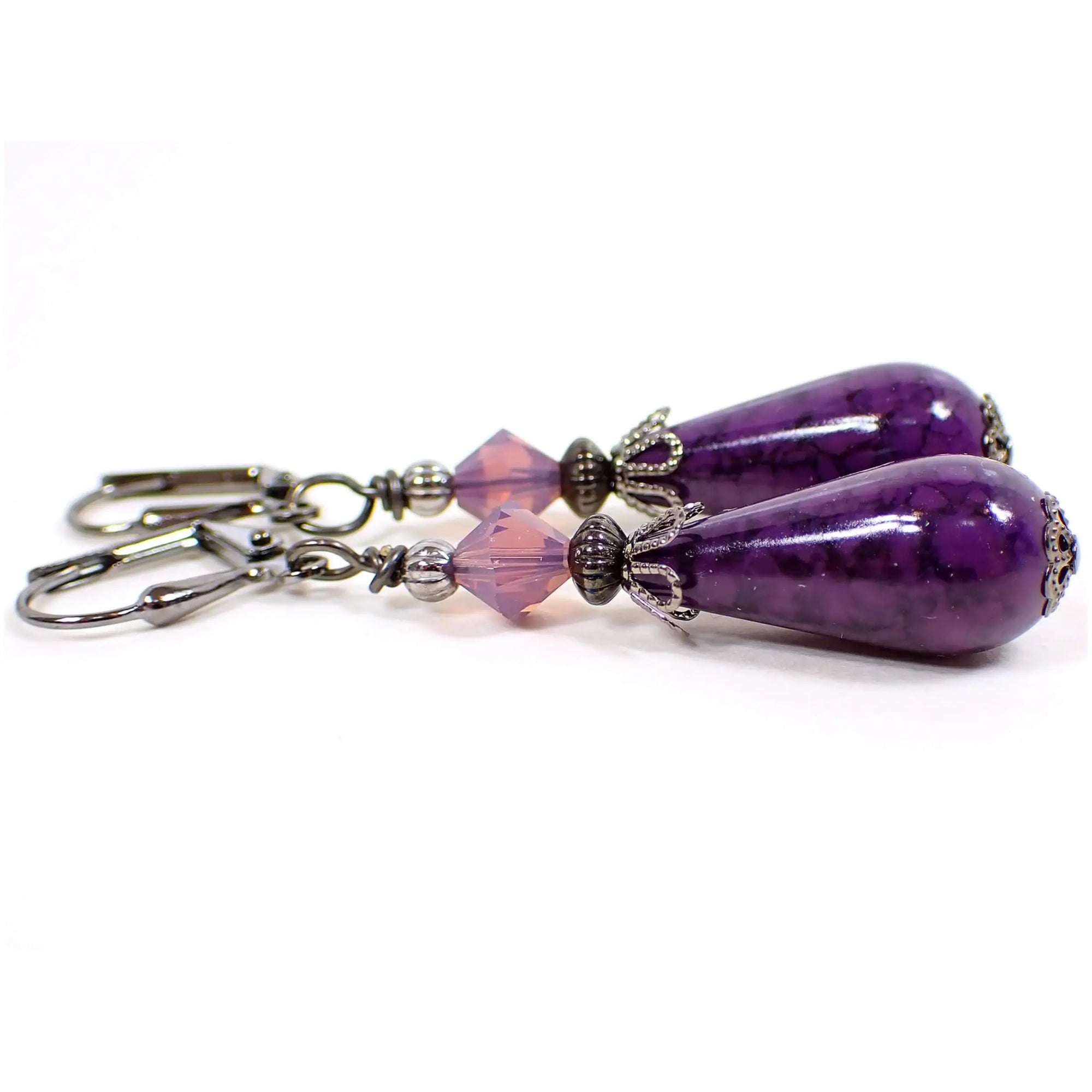 Side view of the handmade teardrop earrings with vintage German acrylic beads. The metal is gunmetal gray in color. There are semi translucent light purple glass crystal faceted beads at the top. The bottom acrylic beads are teardrop shaped and have a marbled pattern with shades of dark purple.