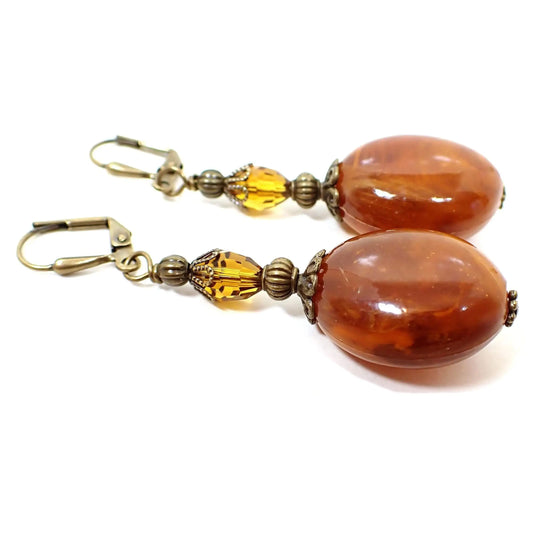 Side view of the handmade vintage beaded earrings. The top vintage beads are oval faceted glass crystals in a citrine orange color. The bottom beads are large oval acrylic beads with marbled swirls of orange, yellow, and brown.