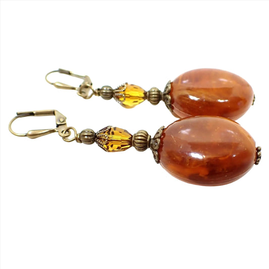 Side view of the handmade vintage beaded earrings. The top vintage beads are oval faceted glass crystals in a citrine orange color. The bottom beads are large oval acrylic beads with marbled swirls of orange, yellow, and brown.