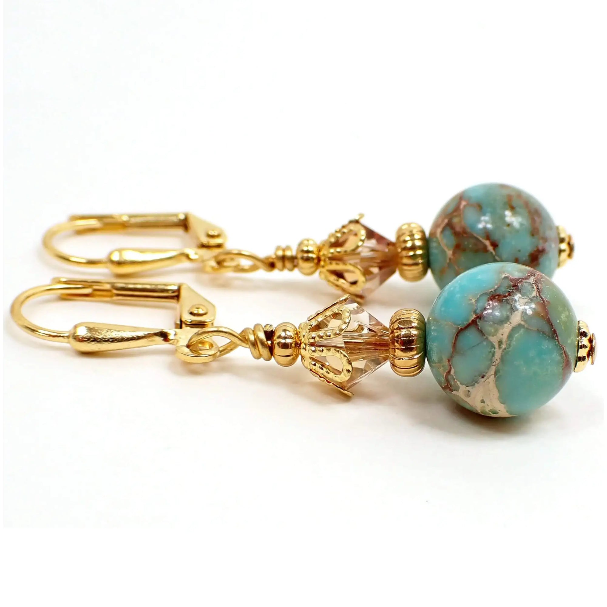 Side view of the handmade sea sediment jasper earrings. The metal on the earrings are gold plated. There are light champagne peach color faceted glass crystal beads at the top. The bottom beads are round and primarily aqua blue in color with marbled streaks of off white cream and shades of brown. There is a hint of red as well.