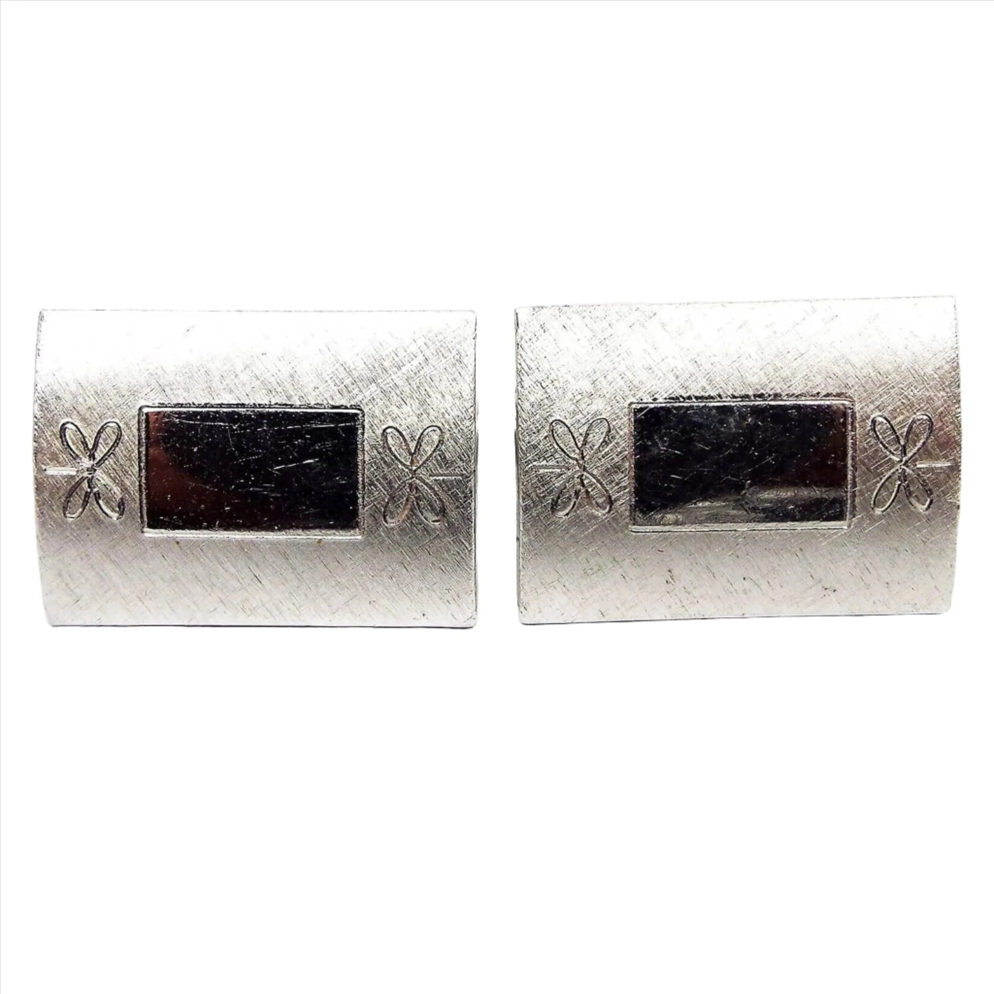 Front view of the Mid Century vintage Anson cufflinks, The metal is silver tone in color. They are rectangle shaped with another rectangle in the middle. The outer edge is brushed matte silver tone with an etched flower design on each side.