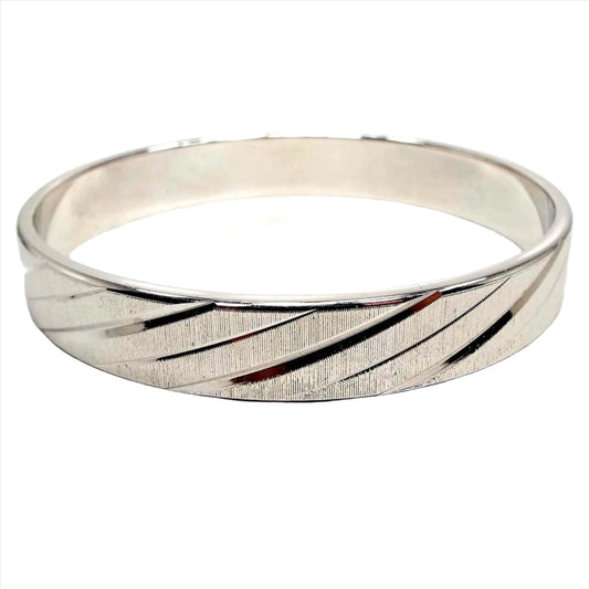 Angled side view of the retro vintage Monet bangle bracelet. The outside has a matte textured surface with tiny ridges. There is a diagonal cut line design all the way around. The inside of the bangle is smooth.